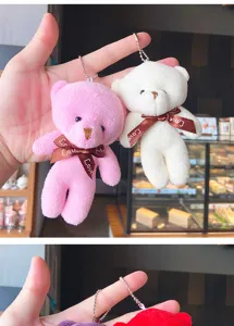 Close-up detail of cute plush bear keychain pendant with ribbon bow and metal ball chain.