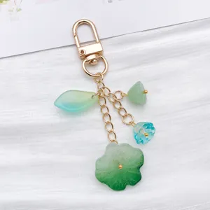 Porte-clés en métal doré avec des charms transparents verts et bleus en forme de feuille.