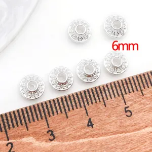 Close up of silver metal UFO spacer beads with detailed flower pattern for DIY jewelry.