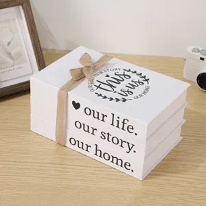 Close-up of white decorative fake book set with burlap bow and cozy English typography for desktop decor.