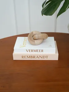 Close-up detail of decorative fake books with gold lettering and a wooden link knot on table.
