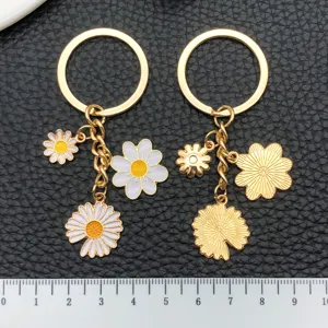 Set portachiavi in lega dorata con margherite in smalto e ciondoli metallici goffrati.