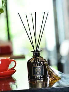 Gros plan d'un flacon de diffuseur en verre noir avec bâtonnets noirs et gland doré, élégant décor.