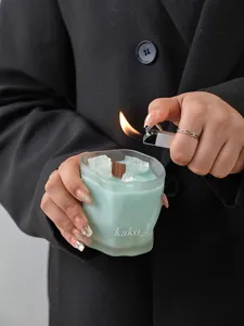 Close-up detail of frosted crystal scented candle with blue wax and wooden wick being lit.
