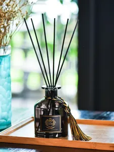 Gros plan de la bouteille de diffuseur de parfum en verre noir avec bâtonnets et pompon.