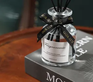 Detail view of glass reed diffuser bottle with black sticks and ribbon for home decor.