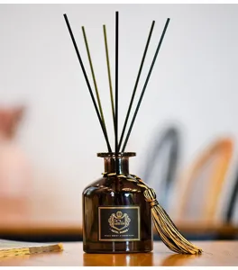 Close-up detail of reed diffuser bottle with black sticks and gold tassel for home decor.
