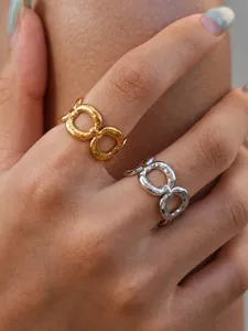 Dettaglio in primo piano di anello geometrico con finiture in metallo lucido oro e argento.