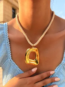 Detailopname van een grove geometrische gouden hanger ketting met dik touwketting.