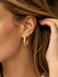 Close-up detail shot of a stylish gold-plated J-shaped hoop earring encrusted with sparkling crystals.