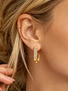 Close-up of golden J-shaped rhinestone paved earrings worn on earlobe with subtle delicate details.