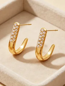 Close-up detail of golden J-shaped rhinestone hoop earrings in beige velvet tray.