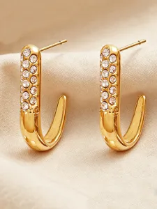 Close-up detail of golden J-shaped stud earrings paved with sparkling crystals on fabric.
