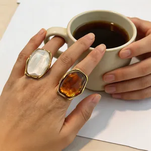 Gros plan détaillé de bagues rétro en résine ambre et blanche portées sur la main.