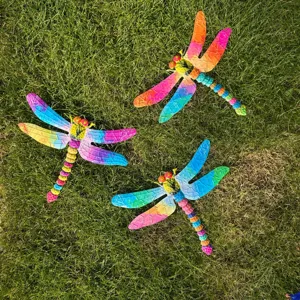 Primo piano di decorazioni di libellule in metallo colorato su erba verde, dettaglio giardino.
