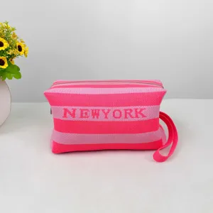Pochette de maquillage rayée en tricot rose détaillée avec le texte NEWYORK et dragonne.
