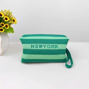 Détail de la pochette en tricot vert avec rayures, texte NEWYORK, fermeture éclair et dragonne.