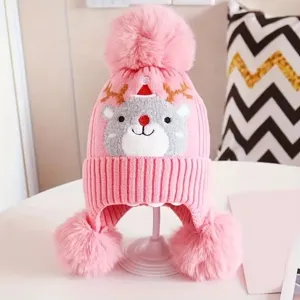 Childrens pink knit beanie winter hat with reindeer pattern, cute pom pom earflap design.