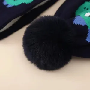 Detailed view of kids winter warm knitted hat with plush pom pom and cute dinosaur jacquard.