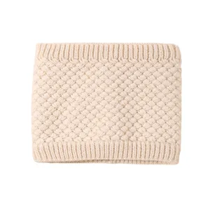 Primo piano dello scaldacollo in maglia beige con motivo intrecciato e colletto a costine.