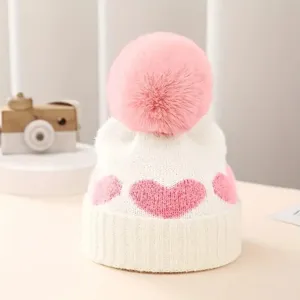 Close-up detail of cute baby knit beanie with pink heart pattern and large fluffy pompom.