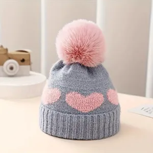 Baby knit hat detail showing cute pink heart pattern, cozy pom pom and soft texture.