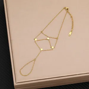 Primo piano dettaglio del bracciale da mano in acciaio dorato con ciondoli quadrati geometrici.