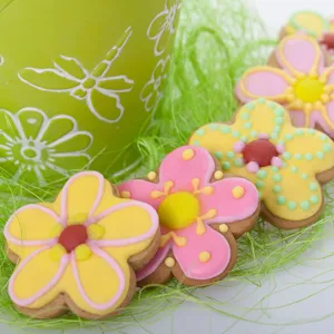 Closeup of colorful decorated spring flower cookies arranged neatly on green Easter grass.