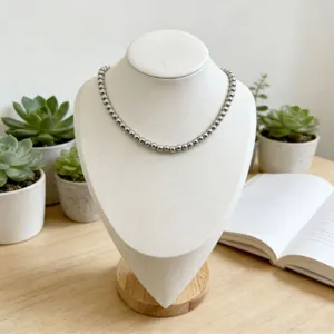 Gros plan détaillé d'un collier de perles en acier inoxydable argenté sur un buste blanc.
