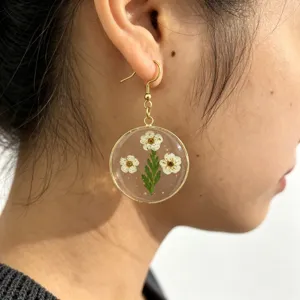 Close-up detail of resin pressed daisy flower pendant earring, elegant botanical style drop ear hook.
