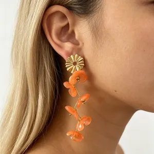 Long floral resin drop earrings detail view, golden metal and orange petals, elegant style.