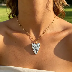Detailed shot of a gold paperclip chain necklace with a textured silver heart pendant.