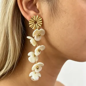 Long floral drop earrings featuring white resin petals and gold-toned metal design details.