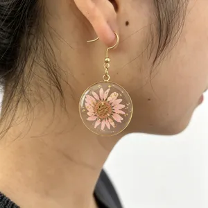 Close-up of elegant resin round earrings featuring dried pink daisy flowers and gold flakes.