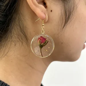 Detailed close-up of a gold-plated resin round pendant earring with a dried red rose.