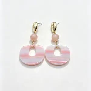 Détail rapproché des boucles d'oreilles pendantes en résine aux rayures roses et blanches.