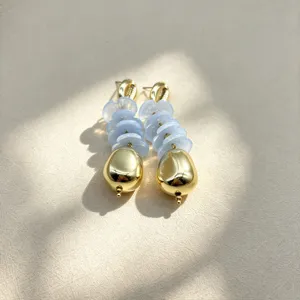 Detailed shot of trendy geometric flower earrings featuring light blue layered beads and gold drops.
