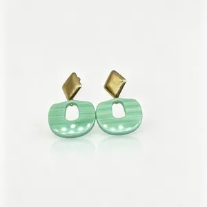 Close-up detail of geometric resin earrings with gold rhombus and mint green pendant.