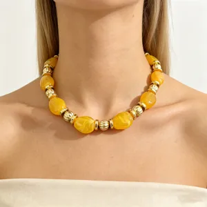 Close-up detail of the chunky yellow resin and gold metal bead statement necklace worn on neck.
