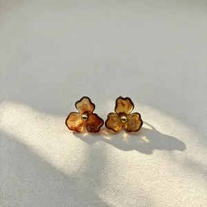 Close-up of amber resin flower stud earrings featuring a chic golden bead center detail.