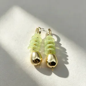 Close-up view of vintage geometric flower drop earrings with pale green discs and gold charm.