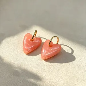 Gedetailleerd overzicht van roze hars hart oorbellen met gouden ringen, elegant ontwerp.