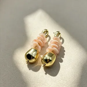 Detailed shot of stylish stacked shell disc and gold teardrop drop earrings in natural sunlight.