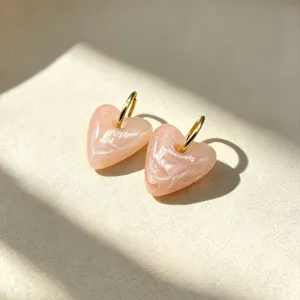 Detailopname van stijlvolle roze hars hart oorbellen met gouden roestvrijstalen ringen.