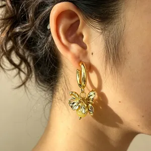 Close-up detail of metallic flower pendant hoop earrings with yellow bead accent fashion style.