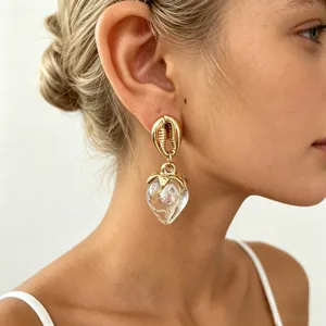 Gros-plan des boucles d'oreilles coquillage doré et pendentif fraise en acrylique transparent.