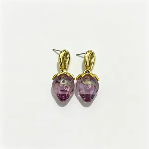 Gros plan détail des boucles d'oreilles fraise violette, design clou coquillage plaqué or.