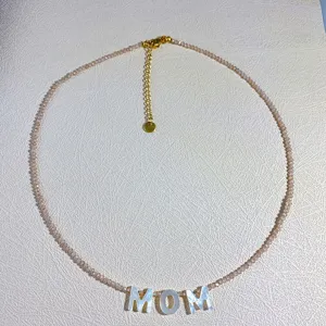 Vista detallada de collar gargantilla de cuentas delicadas con colgante de letra MOM concha.