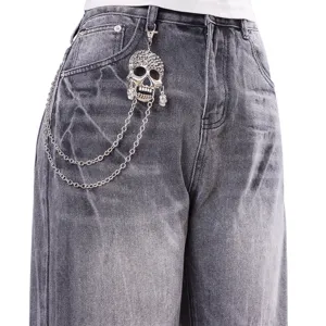 Dettaglio catena teschio punk su jeans grigi slavati, catena da vita rock streetwear.