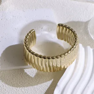Close-up view of a wide gold textured metal cuff bracelet detail on a white geometric prop.